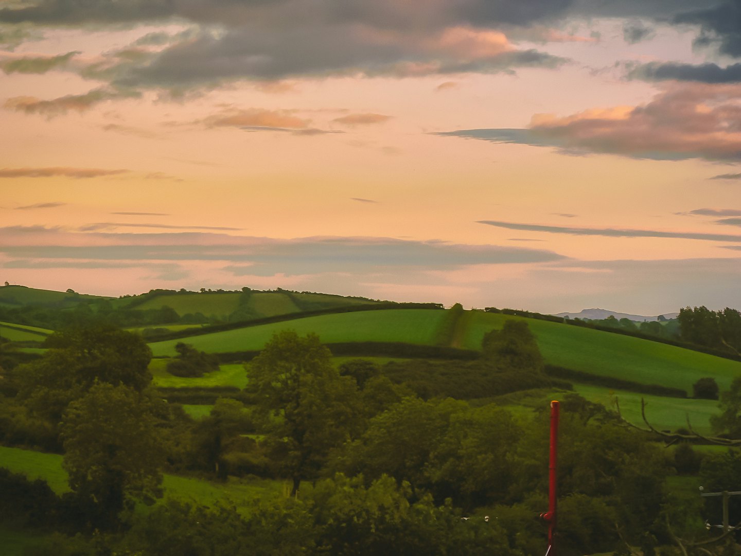 Rolling green hills and trees under a colorful sunrise sky.
