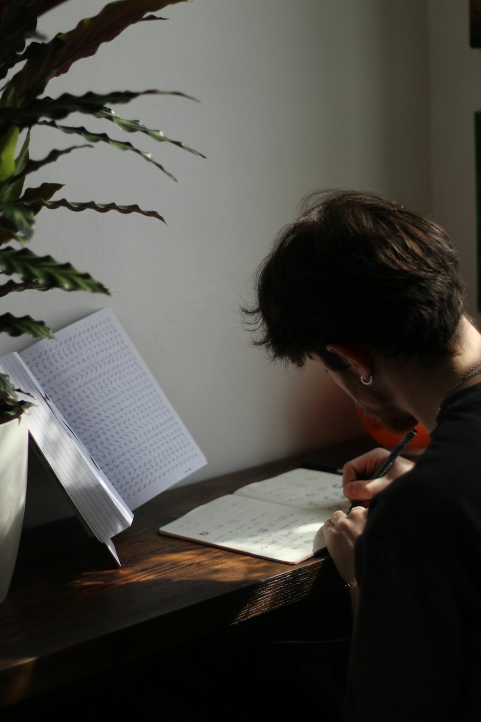 Person writing and sketching in a notebook at a desk.